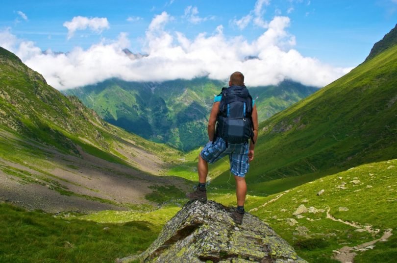 young-male-backpacker-standing-on-a-hill-with-a-rocky-mountain-green-background.jpg